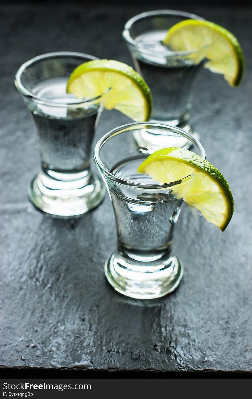 Vodka in shot glasses on black stone background, iced strong drink in misted glass. Vodka in shot glasses on black stone background, iced strong drink in misted glass