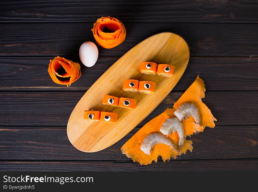 Top view of Japanese tempura shrimp sushi roll without rice wrapped in carrot daikon slices served on wooden plate.