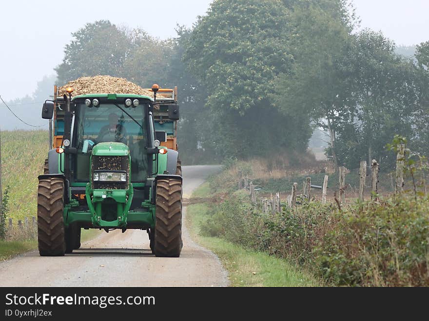 Green tractor with a trailer full of chipped maize travelling along a country road taking the harvest to the farm to store and make silage. Green tractor with a trailer full of chipped maize travelling along a country road taking the harvest to the farm to store and make silage