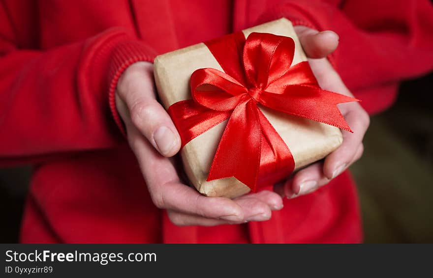 Young woman in red swether holding a gift box wrapped in brown paper and tied with a red ribbon with a bow for a space event.