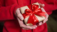 Young Woman In Red Swether Holding A Gift Box Wrapped In Brown Paper And Tied With A Red Ribbon With A Bow For A Space Event. Royalty Free Stock Photos