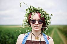 Young Hippie Woman With Short Red Hair, Wearing Boho Style Clothes And Flower Wreath, Standing On Green Currant Field, Posing For Royalty Free Stock Image