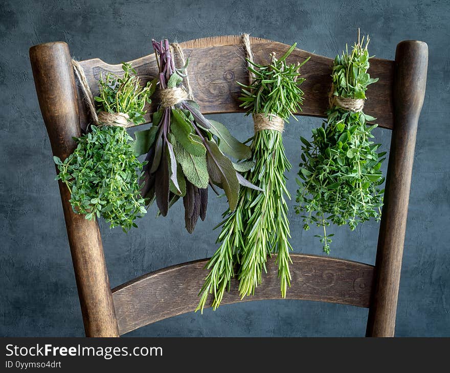 Bunches of herbs hanging on old wooden chair. Thyme, sage, rosemary, oregano