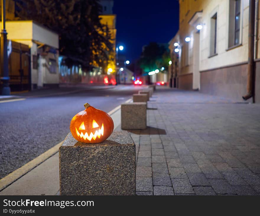 Halloween pumpkin on a deserted city street at night. Blurry colored city lights and old high-rise buildings