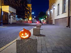 Halloween Pumpkin On A Deserted City Street At Night. Blurry Colored City Lights And Old High-rise Buildings Royalty Free Stock Photos