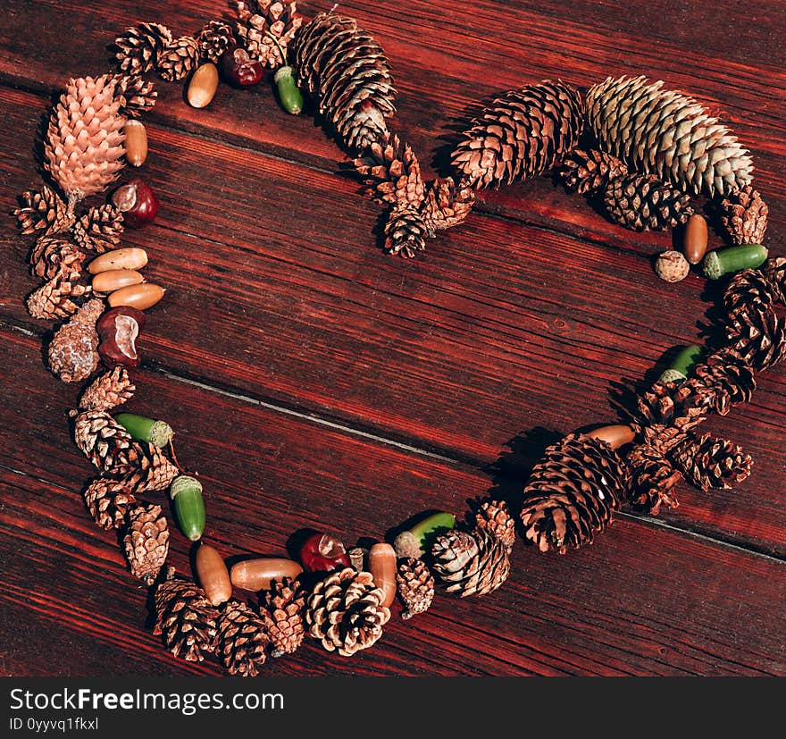 Lots of small pine cones and acorns are in the shape of a heart on the wooden mahogany table. Autumn textured background and plenty of space for text and design. Lots of small pine cones and acorns are in the shape of a heart on the wooden mahogany table. Autumn textured background and plenty of space for text and design