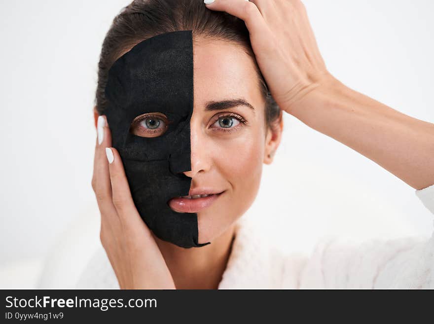 Skin care. Portrait of young girl with black mask posing with hands near her face. Purifying spa treatment, white studio background. Skin care. Portrait of young girl with black mask posing with hands near her face. Purifying spa treatment, white studio background