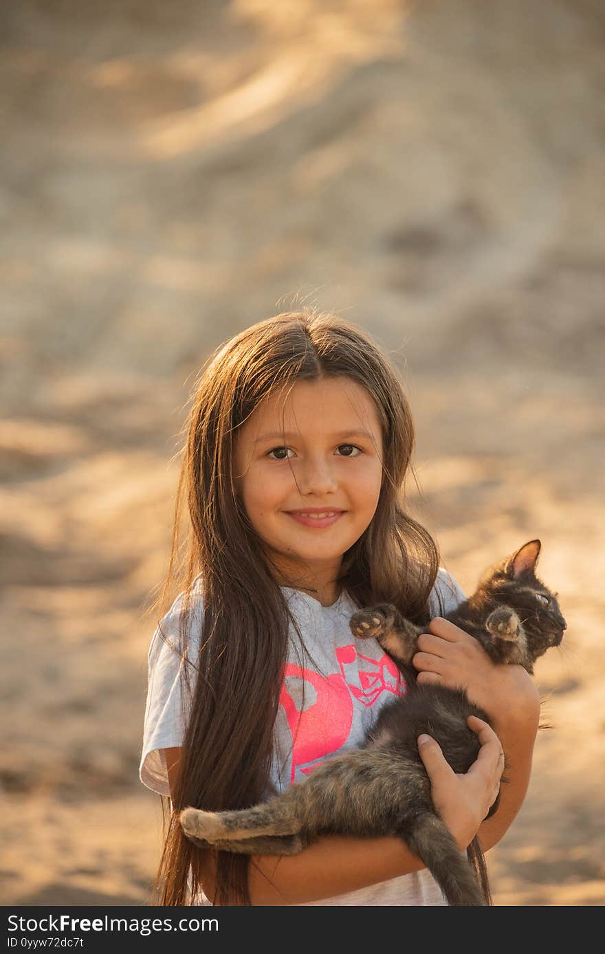 Portrait of adorable child with kitten. Baby girl holding hands a kitten in the light of sunset, pet, friend, lifestyle. Kid playing with a cat