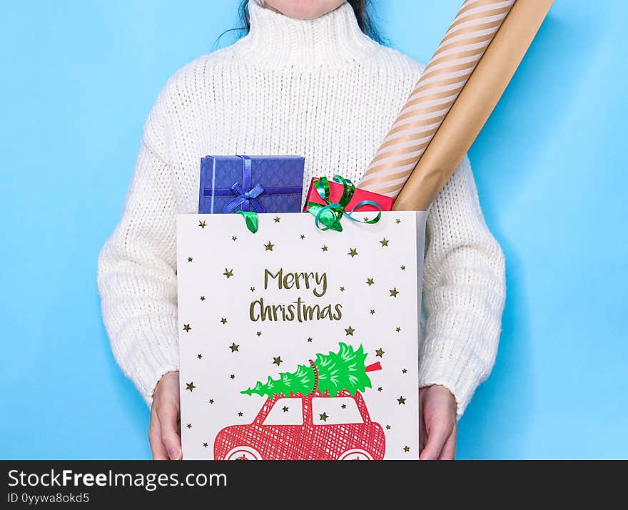 A woman no face in a white knitted sweater holds a gift bag with boxes for Christmas, close-up side view. A woman no face in a white knitted sweater holds a gift bag with boxes for Christmas, close-up side view.