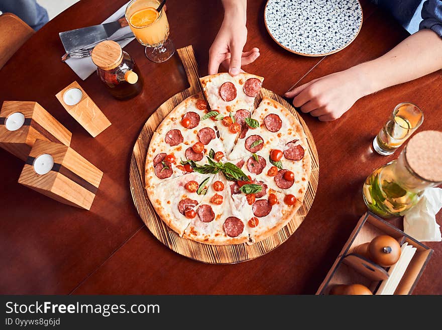 Woman taking slice of pepperoni pizza on red table. Woman taking slice of pepperoni pizza on red table