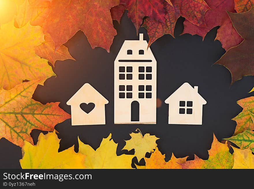 On a black background - three different wooden houses surrounded by autumn leaves. Concept - Autumn sales, year-end sales, affordable housing, mortgage discounts, real estate investments