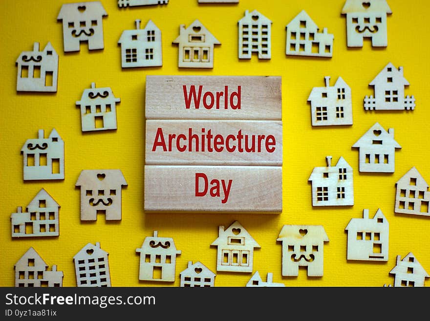 Wooden blocks form the words `World Architecture Day`, miniature wooden houses. Beautiful yellow background, copy space. Busines