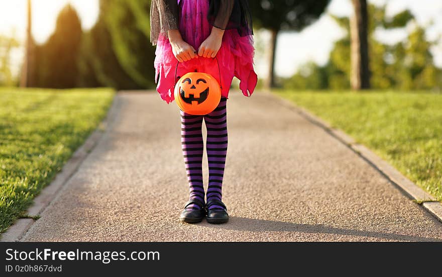 Unrecognizable girl in witch costume and with trick or treat basket standing on asphalt path during Halloween celebration in park. Unrecognizable girl in witch costume and with trick or treat basket standing on asphalt path during Halloween celebration in park