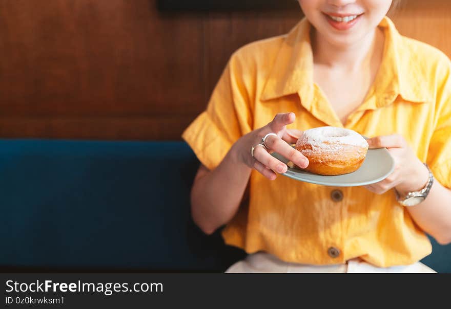 Woman smile and wearing yellow shirt holding and showing a pale green plate of sugar glazed donut in a modern cafe. Enjoyment female lifestyle. Focus on hand and donut.