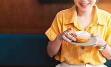 Woman Smile And Wearing Yellow Shirt Holding And Showing A Pale Green Plate Of Sugar Glazed Donut In A Modern Cafe. Stock Photography