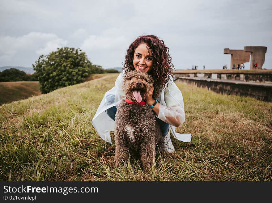 A pretty young woman with a white rain jacket petting and playing with her Spanish water dog in a rainy day in the north of Spain