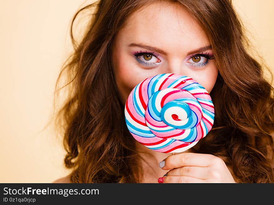 Woman attractive girl colorful eyes make up holding big lollipop candy in hand, covering her face. Sweet food and enjoying concept. Studio shot on bright. Woman attractive girl colorful eyes make up holding big lollipop candy in hand, covering her face. Sweet food and enjoying concept. Studio shot on bright