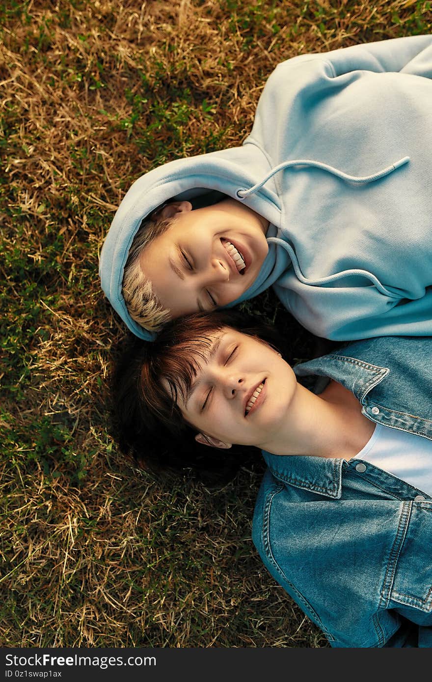 Top view of happy lesbian couple lying on the grass in summer park. Women in love smiling with closed eyes while spending time together outdoors. Relationships, LGBT. Selective focus. Vertical shot