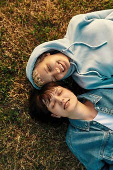 Top View Of Happy Lesbian Couple Lying On The Grass In Summer Park. Women In Love Smiling With Closed Eyes While Stock Photo