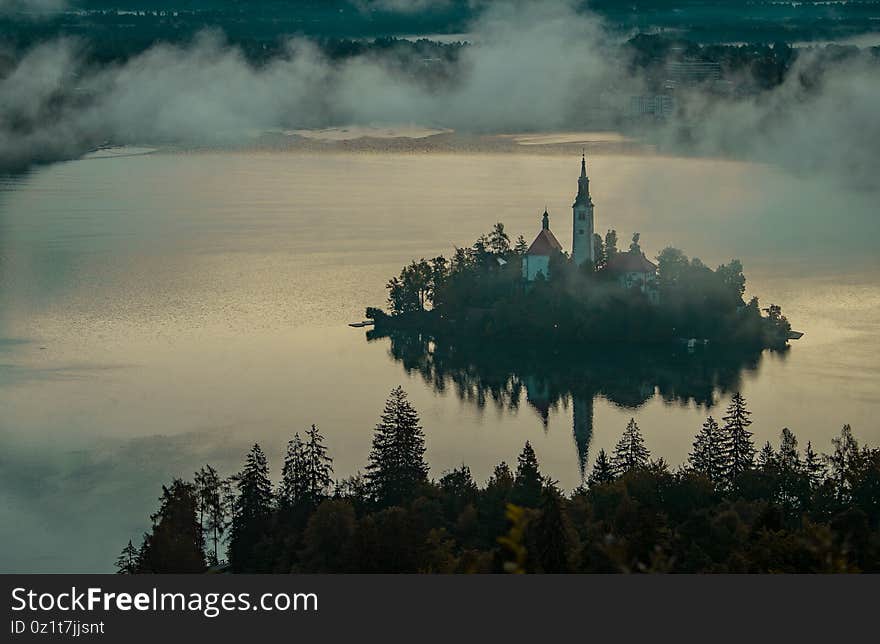 Panoramic photo of lake Bled island with church on a cold hazy foggy early autumn morning from Ojstrica vantage point. Visible