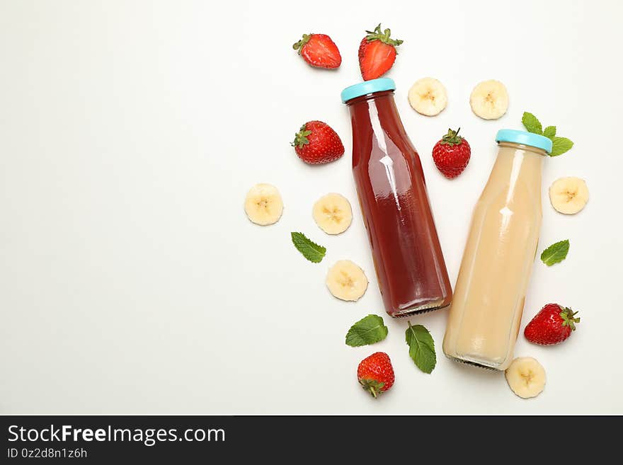 Bottles with strawberry and banana juices on white background