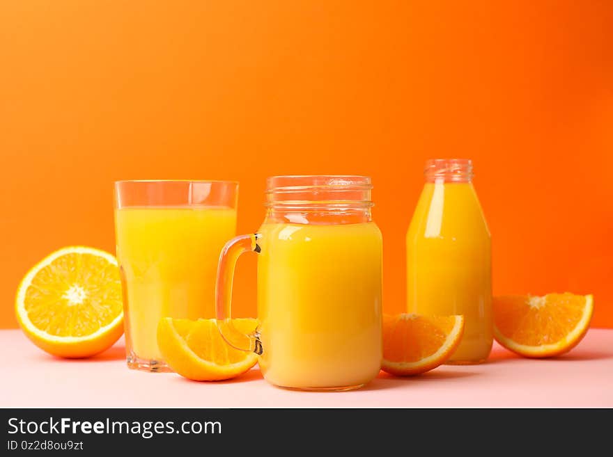 Glass jars with orange juice on pink table