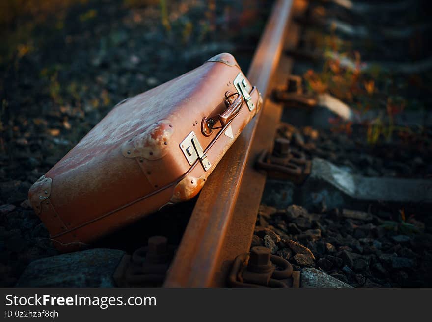 An old orange forgotten suitcase lies near the rusty railway on a sunny autumn day. Waiting for a trip. Hitchhiking