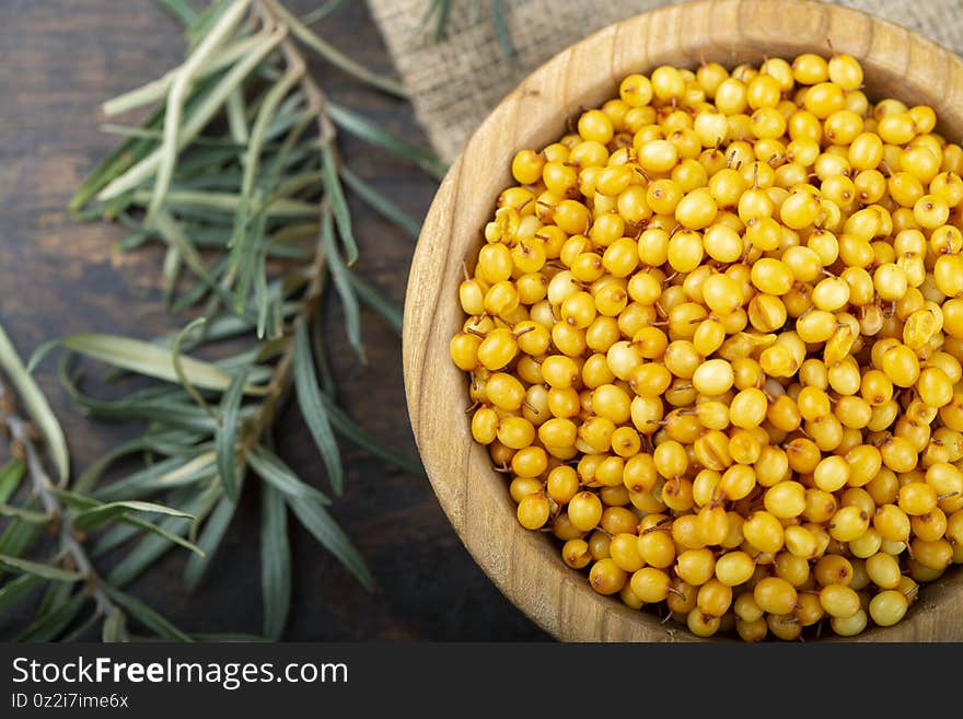 Sea buckthorn. Fresh ripe berry in wooden bowl with leaves on wood background. medicinal berries. Top view