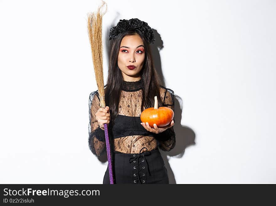 Image of sassy witch in gothic lace dress, holding broom and pumpkin, looking at upper left corner with halloween banner