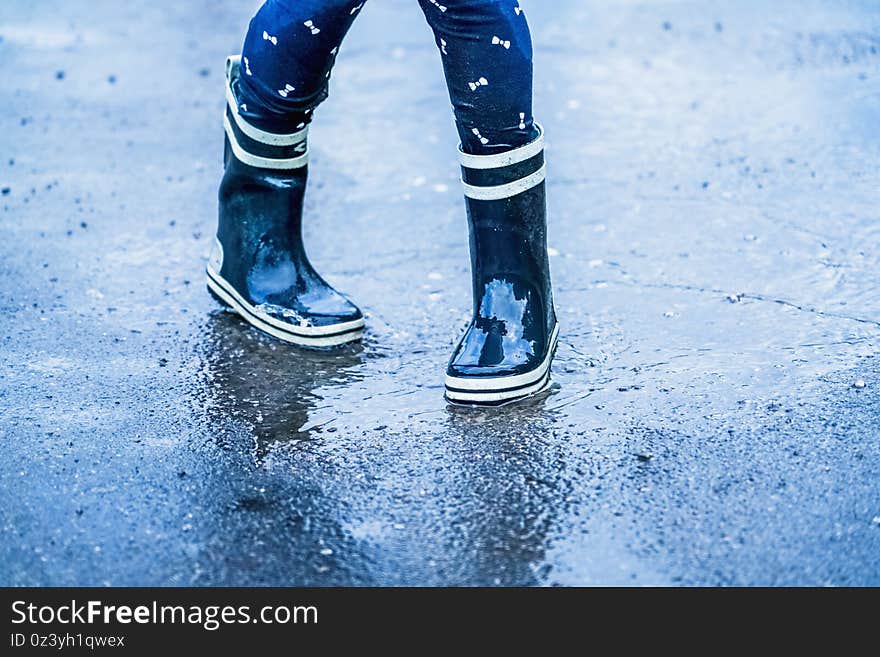 Autumn rainy weather. Child wearing rain boots dancing in puddles after rain