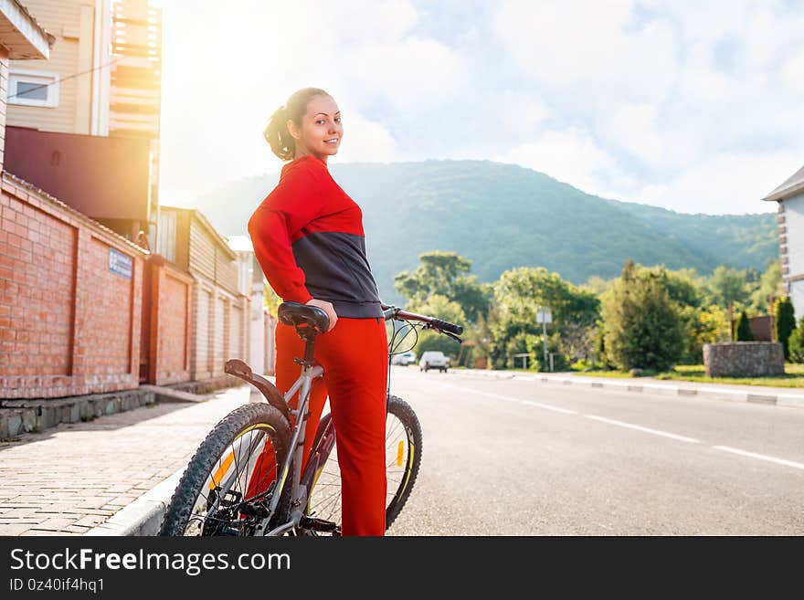 Sports lifestyle. Beautiful smiling young woman in sportswear posing sitting on a Bicycle. Rear view. In the background, an empty