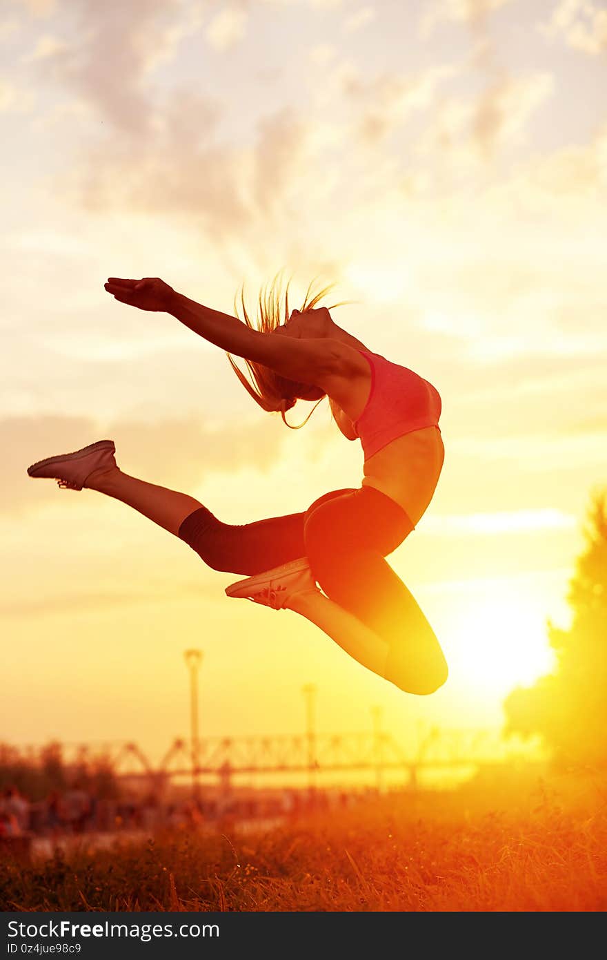 Modern style dancer woman jumping. Dancer silhouette at sunset. Contour of girl on urban city background.