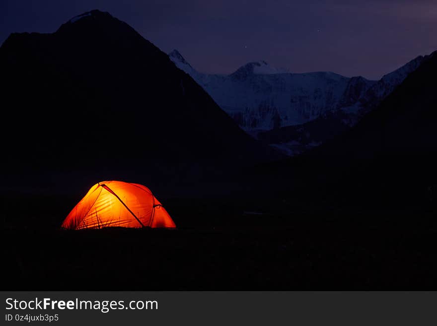 Tent Glowing red under in Belukha Mountain, Altai, a night sky full of stars