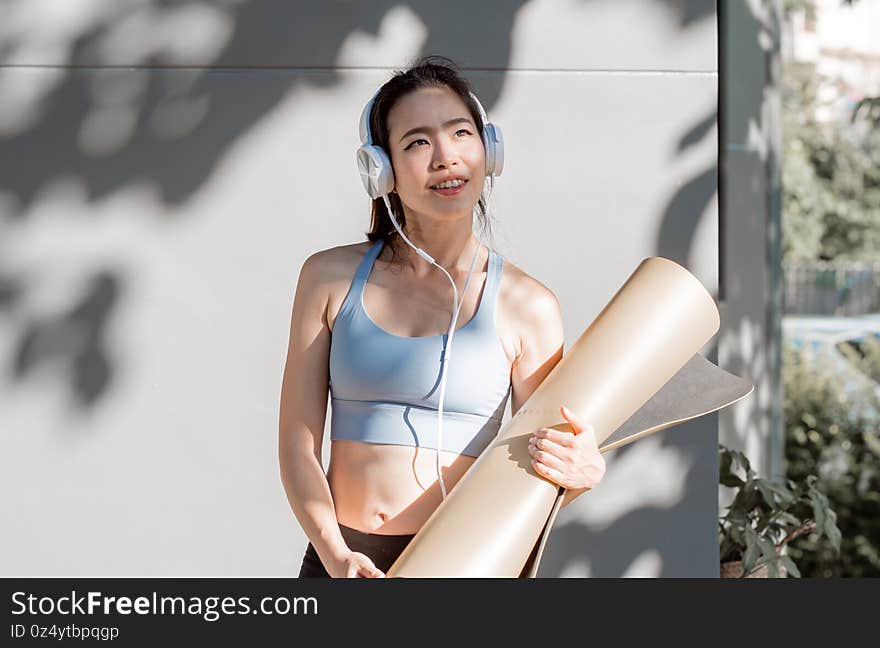 Asian sportive woman listening music and holding yoga mat