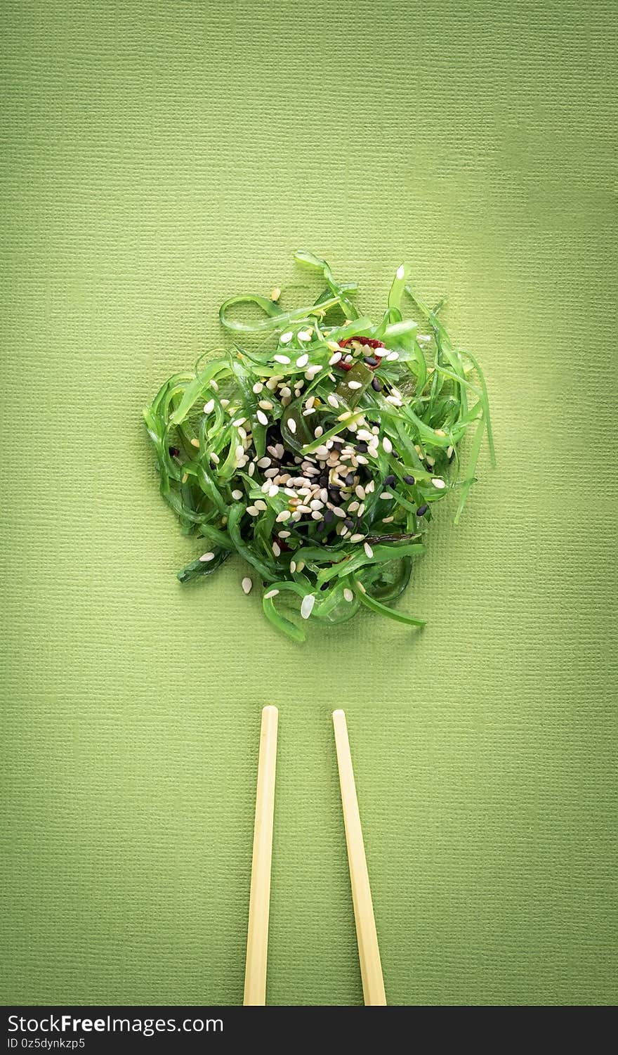 Seaweed salad with sesame seeds on top with chopsticks on a green background, top view