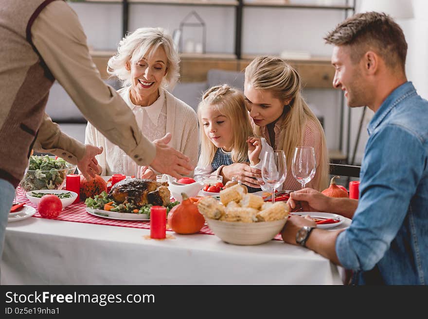 Family members sitting at table and grandfather holding plate with turkey in Thanksgiving day