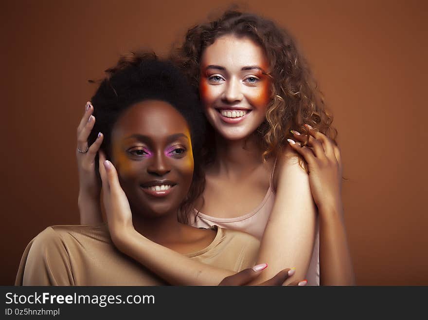 Two pretty girls african and caucasian blond posing cheerful together on brown background, ethnicity diverse lifestyle