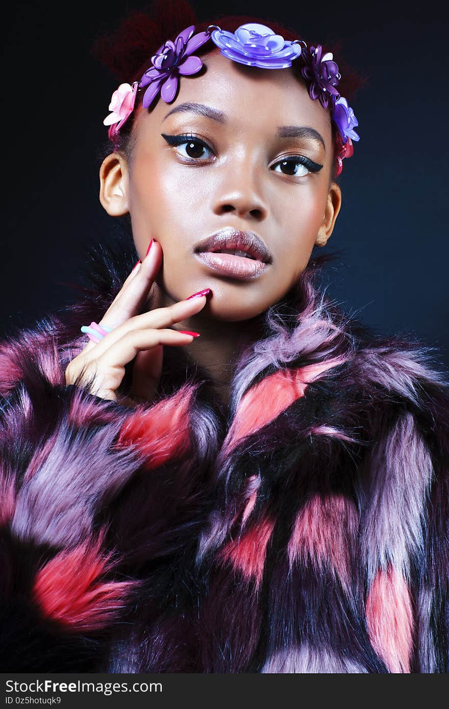 Young pretty african american woman in spotted fur coat and flowers jewelry posing on black background