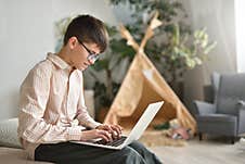 Teenager Boy With Glasses Works In His Laptop Against The Background Of His Room Royalty Free Stock Photos