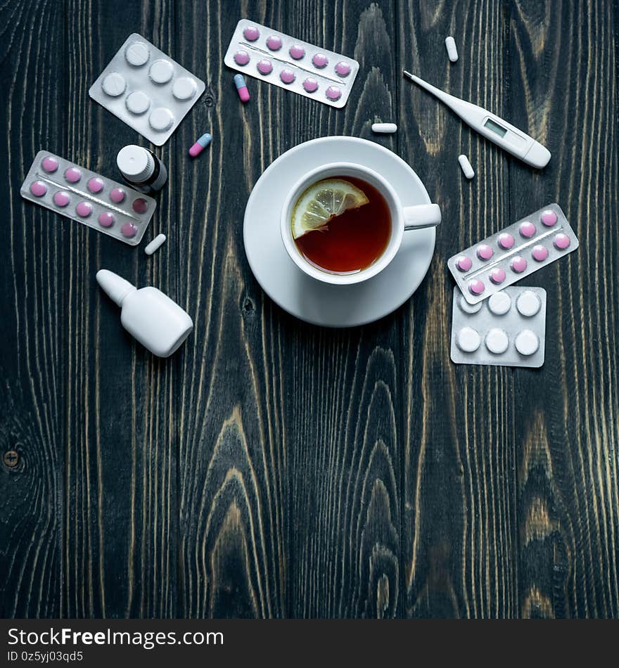 Top view of cup of tea, pills and thermometer on wooden background.