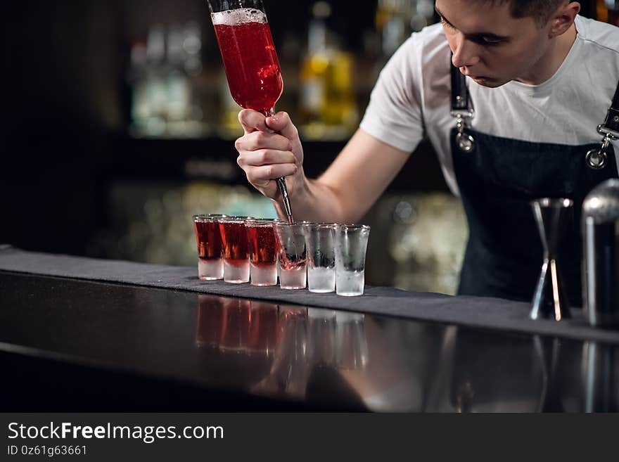 The bartender fills shots with red liquor from a bottle on the bar