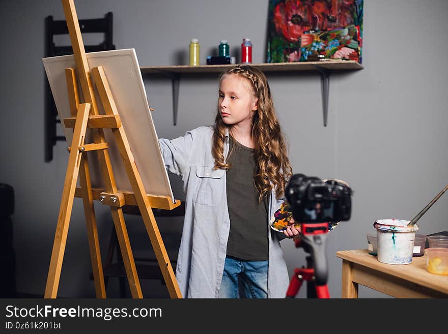 A cute teen artist is recording a story for her video blog in a workshop at an art school.