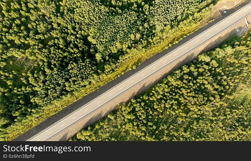 Aerial birds eye view over an empty country road between green forest