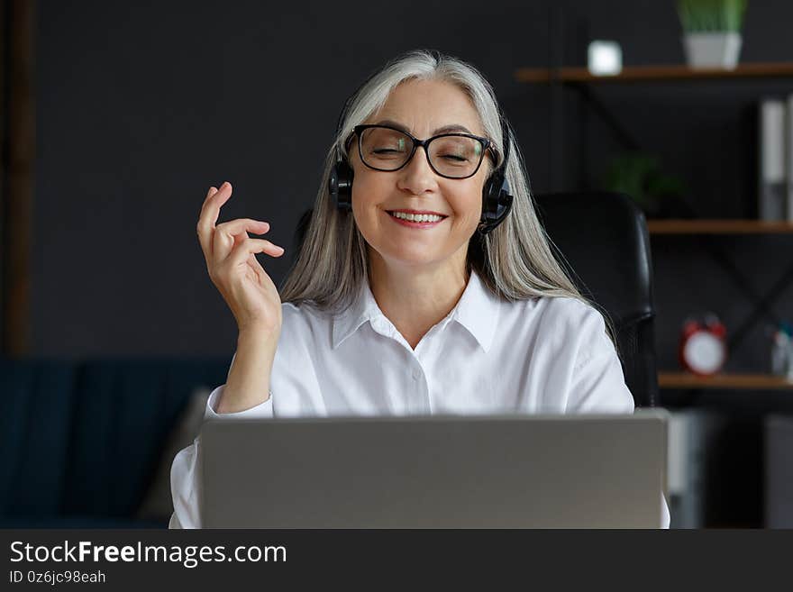 Portrait of smiling grey-haired mature woman using laptop for a online meeting, video call, video conference