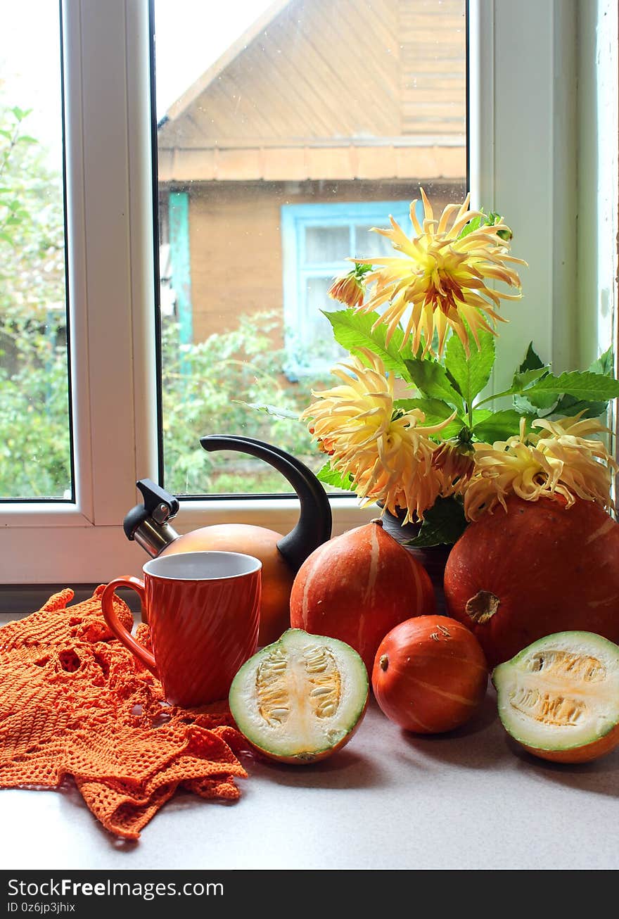 Autumn composition on the kitchen table of ripe pumpkins, orange mug and teapot , a bouquet of yellow dahlias on the background of