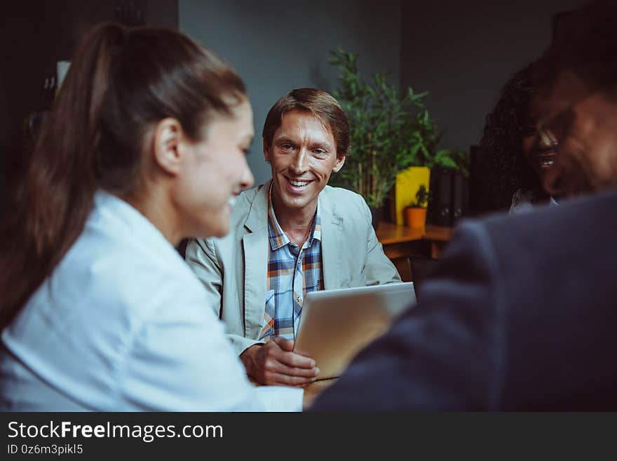 Friendly team of international people brainstorming in office. Diverse group of employees communicating during business meeting. Selective focus on smiling Caucasian business man. Friendly team of international people brainstorming in office. Diverse group of employees communicating during business meeting. Selective focus on smiling Caucasian business man.