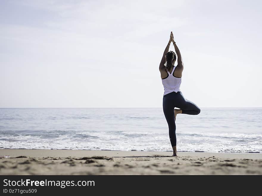 Sporty young woman doing Yoga exercises using a gym mat along the beach in Lisbon, Portugal. Playful woman working as freelance