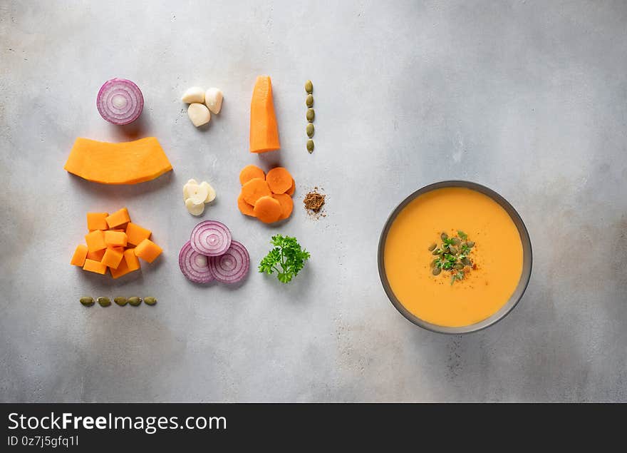 Autumn pumpkin soup in dark bowl and ingredients for cooking.