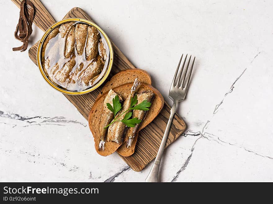 A can with golden sprats in oil and fish sandwiches on wooden board