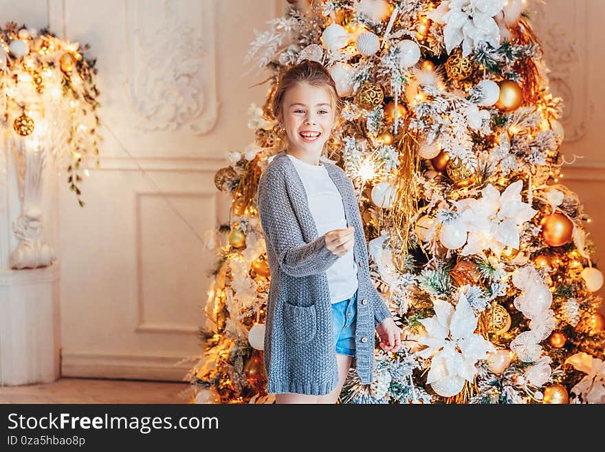 Little girl with sparkler near Christmas tree on Christmas eve at home. Young kid in light bedroom with winter decoration Happy family at home. Christmas New Year december time for celebration concept